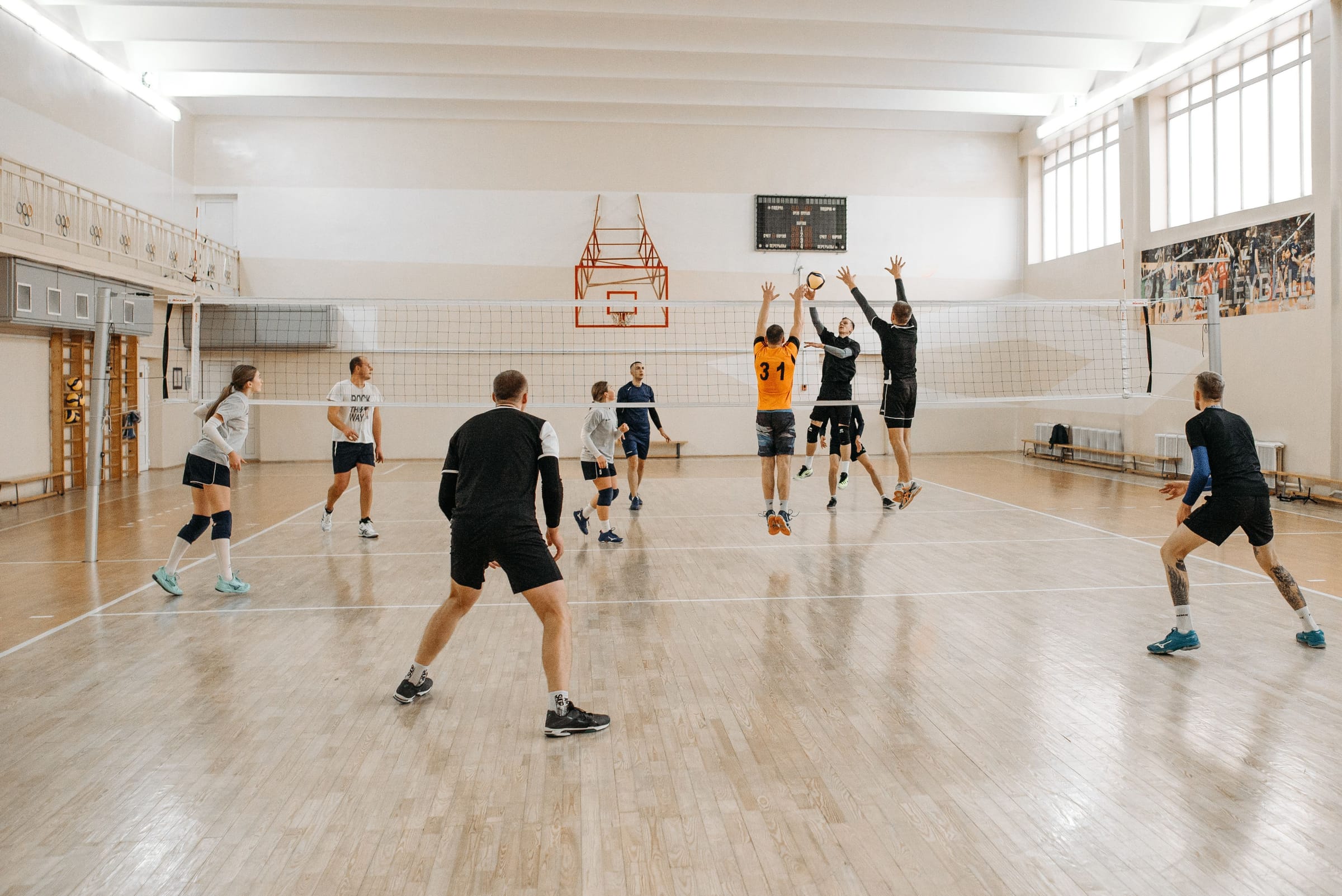 A volleyball match in a bright gym, with players going up for a block at the net